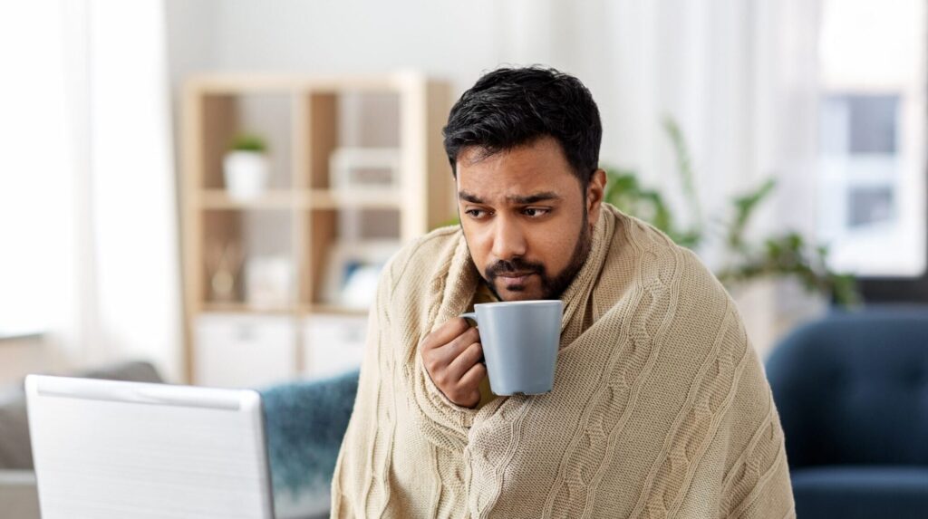 man in blanket with laptop cold home